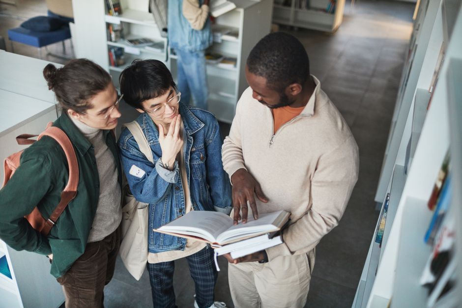 A group of diverse students collaborating over a book in a library setting.